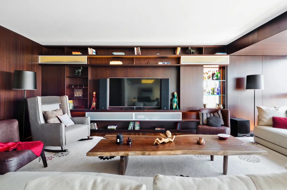 Sala moderna com painéis de madeira escura e móveis cinzas — projeto Departamento Nuñez, por Claudia Faena Studio, em Núñez