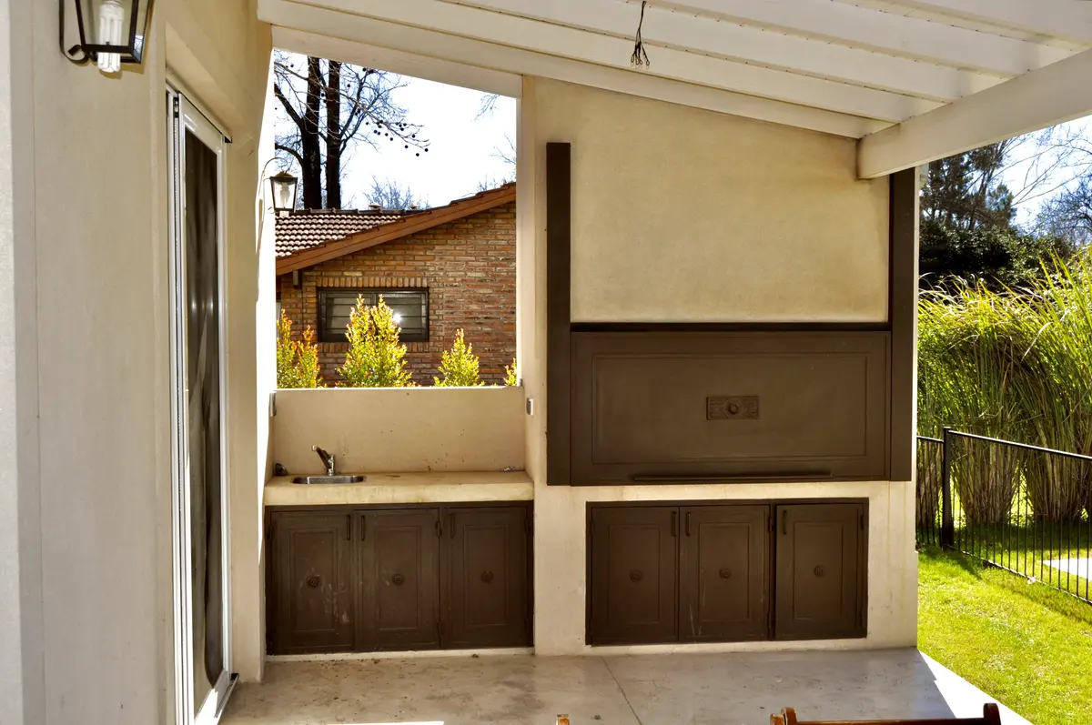 Quincho moderno con parrilla integrada y mesada de madera — proyecto Newman Benavidez, por Marconi Silva Arquitectos, en Benavidez