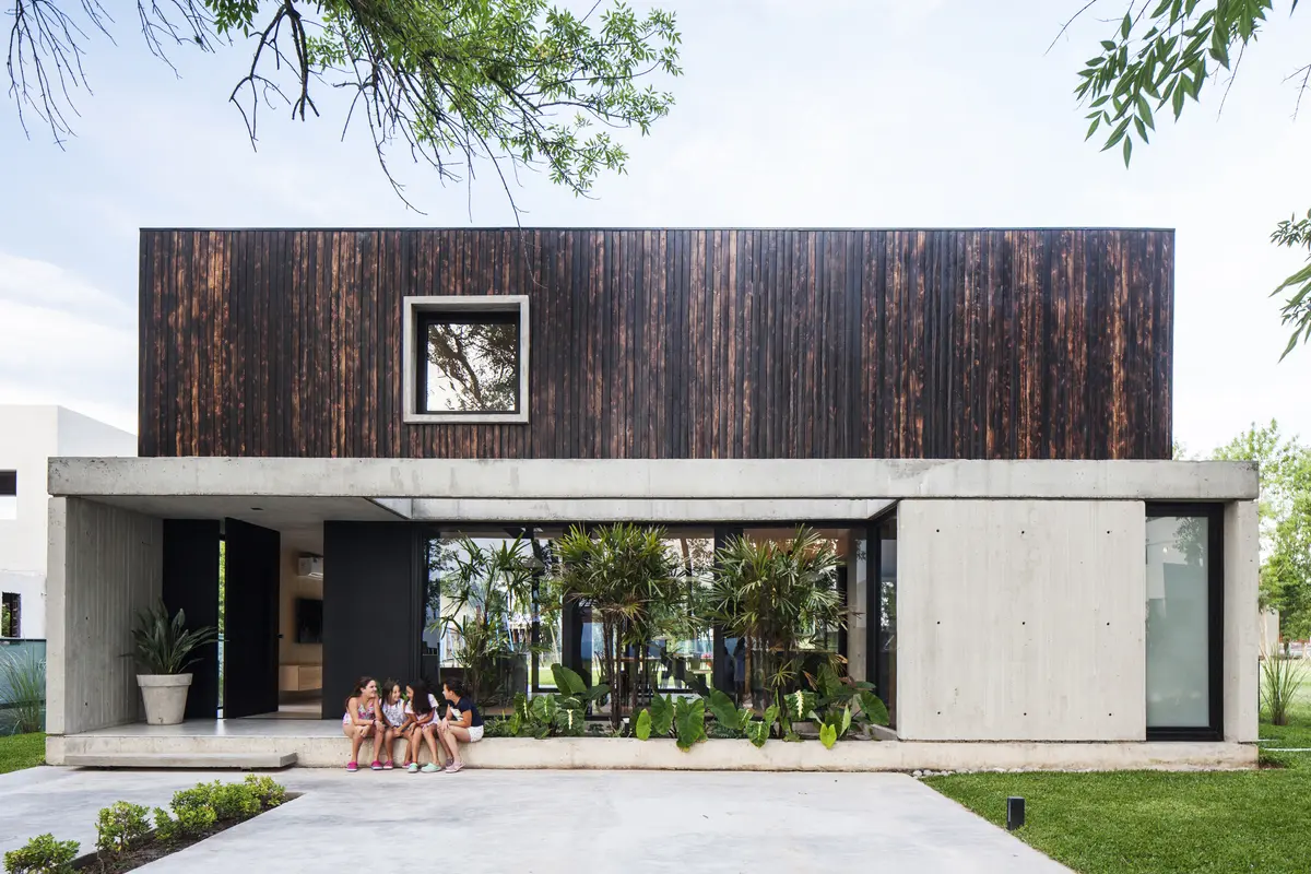 Casa moderna com fachada de madeira escura e grandes janelas — projeto Black House, por V2 Arquitectos, em City Bell