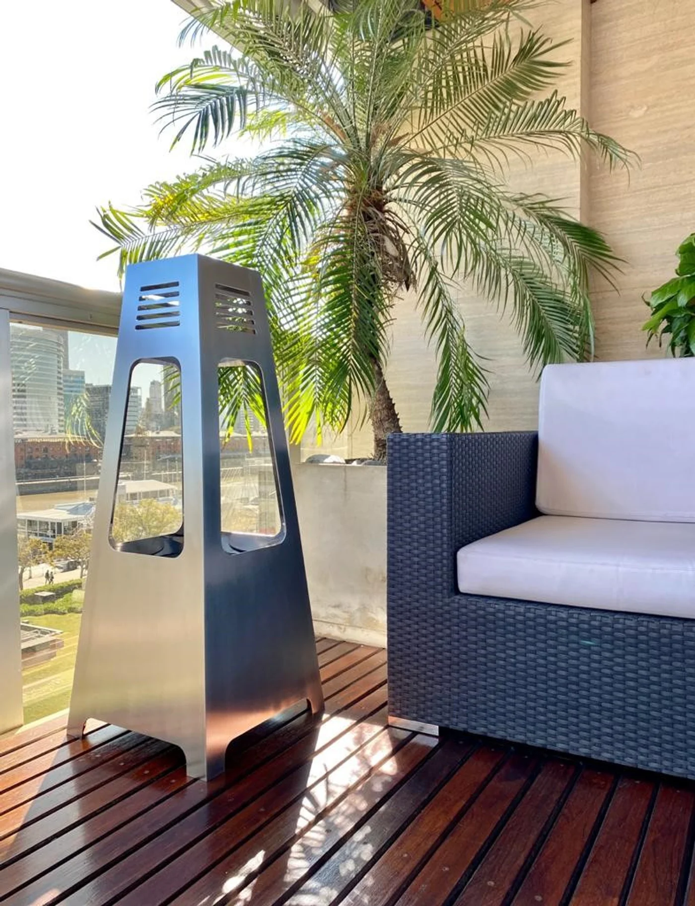 Terraza con deck de madera, sofá gris y calefactor moderno bajo palmera