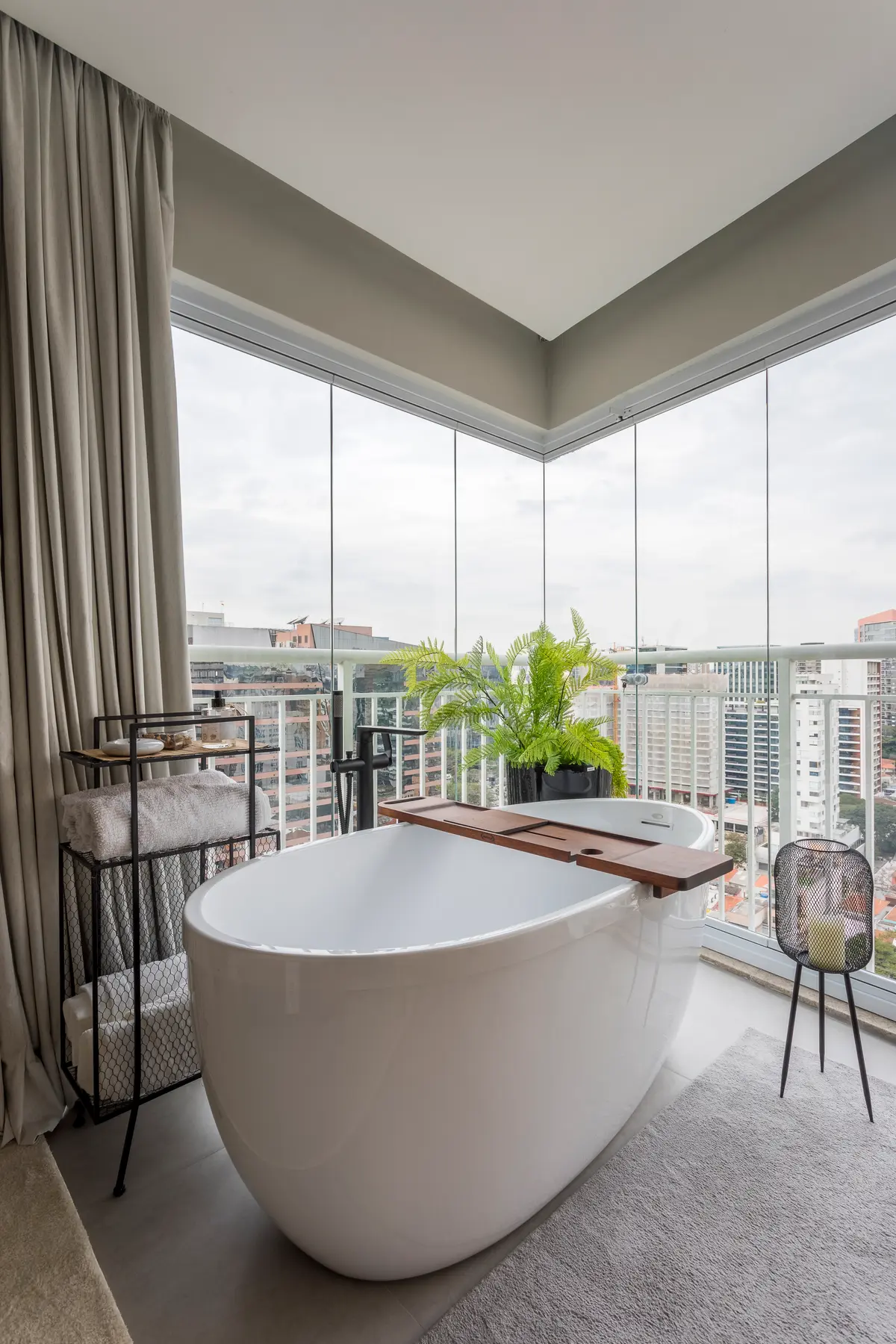 Banheiro moderno com banheira freestanding em varanda envidraçada com vista urbana — projeto Brunno-Fernanda, por Mariana Coser