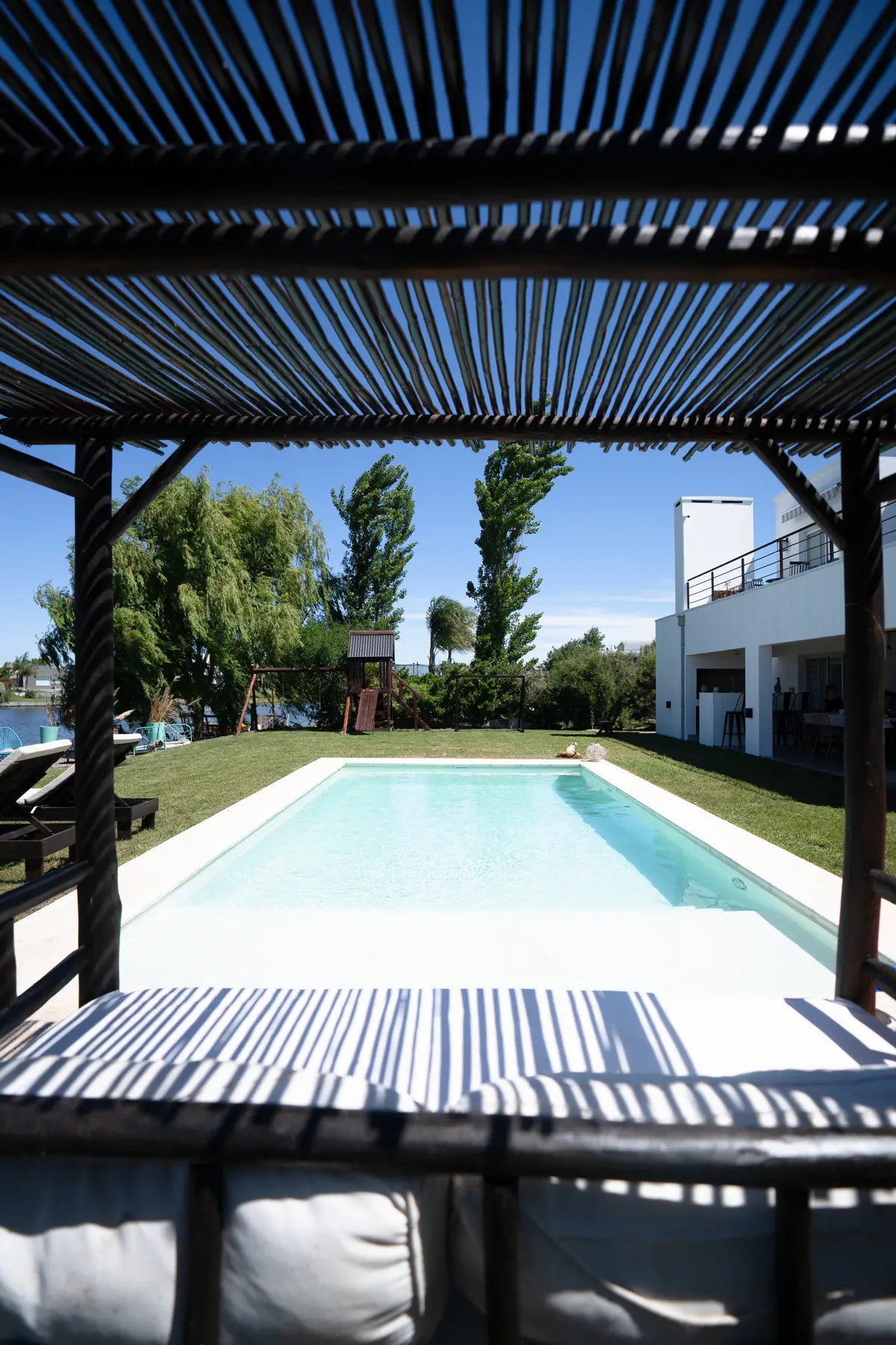 Piscina moderna bajo pérgola con muebles de exterior — proyecto Obra Fachada Nicole, por Arq. Lourdes Yarade Saravia, en Manzanares