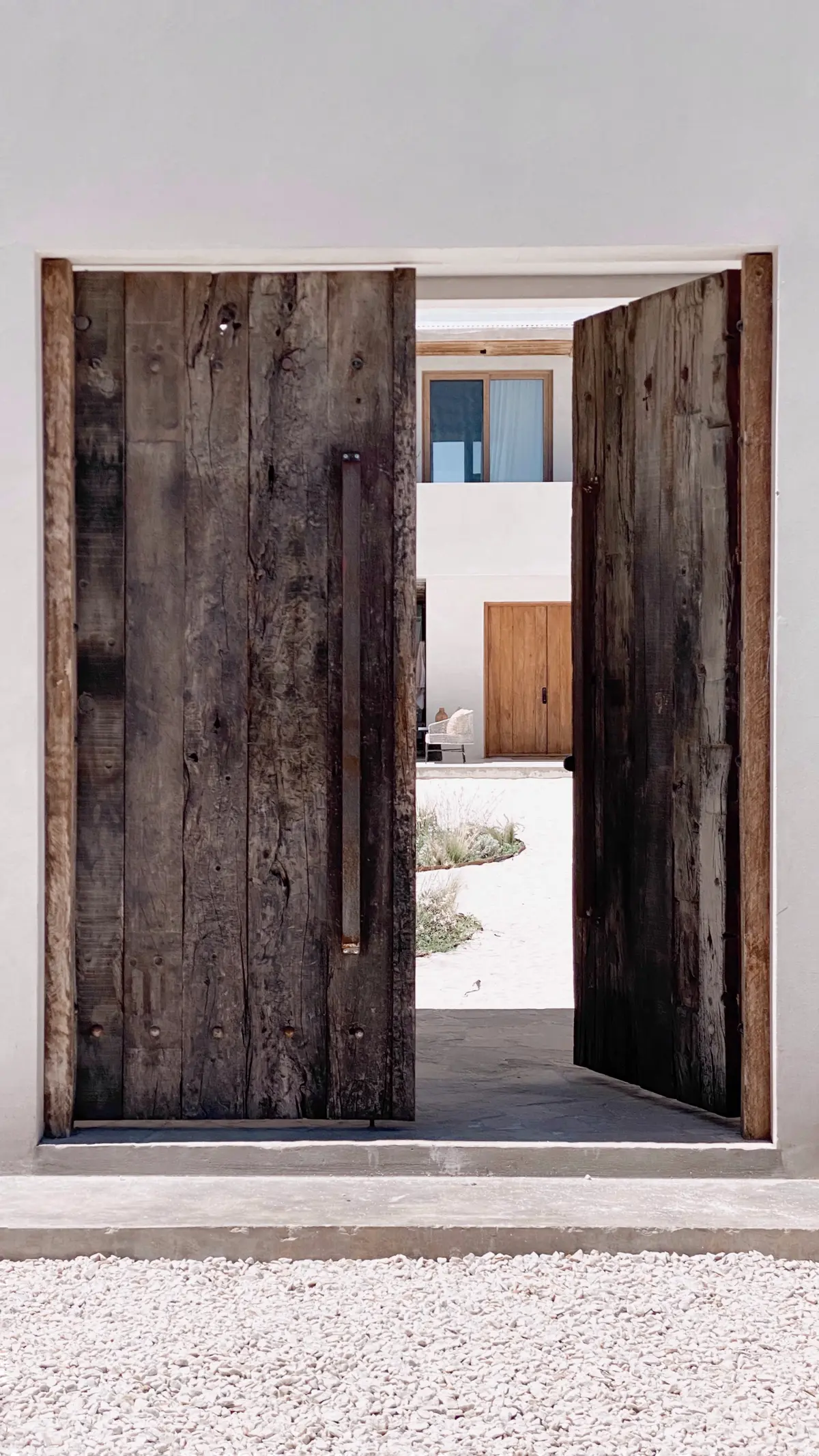 Fachada rústica com grandes portas de madeira e detalhes em concreto — projeto El Refugio, por Grupo Pauta Arquitectura, em Pinamar