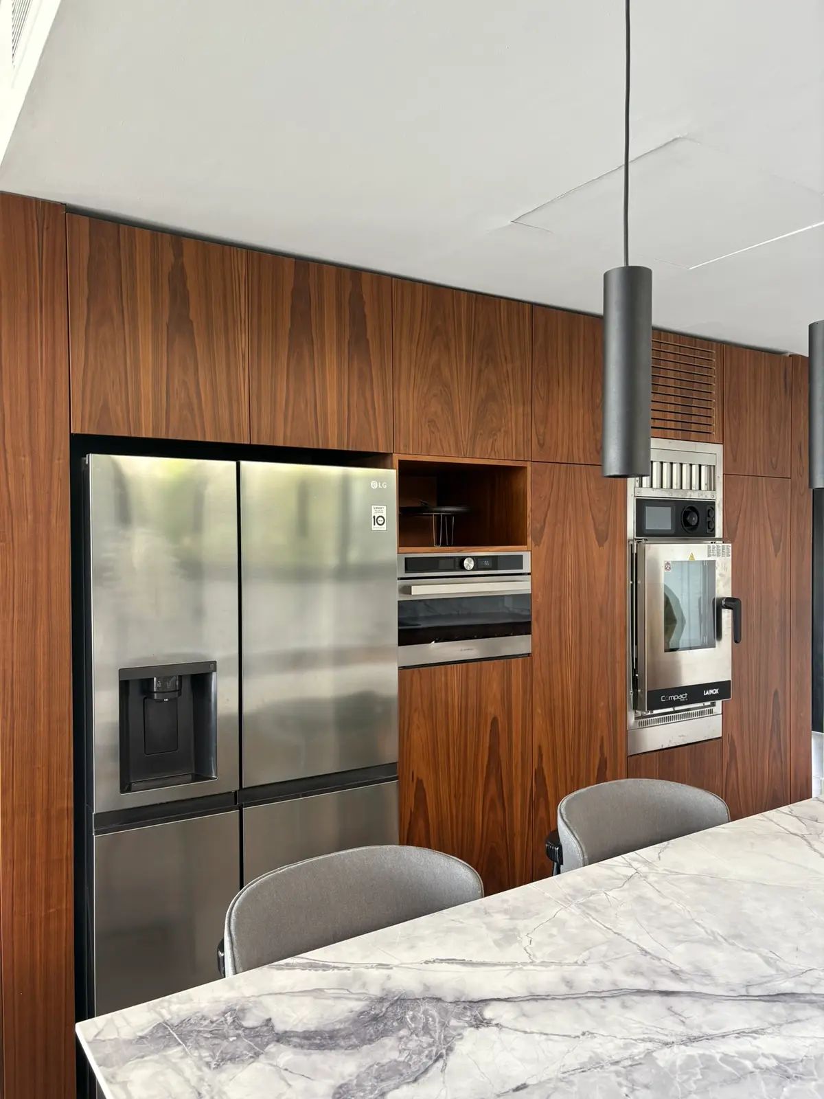 Cocina moderna con paneles de madera, electrodomésticos integrados y luz colgante — proyecto Carpinchos - Estudio Gambotto, por ABEJA CONCEPT, en Nordelta