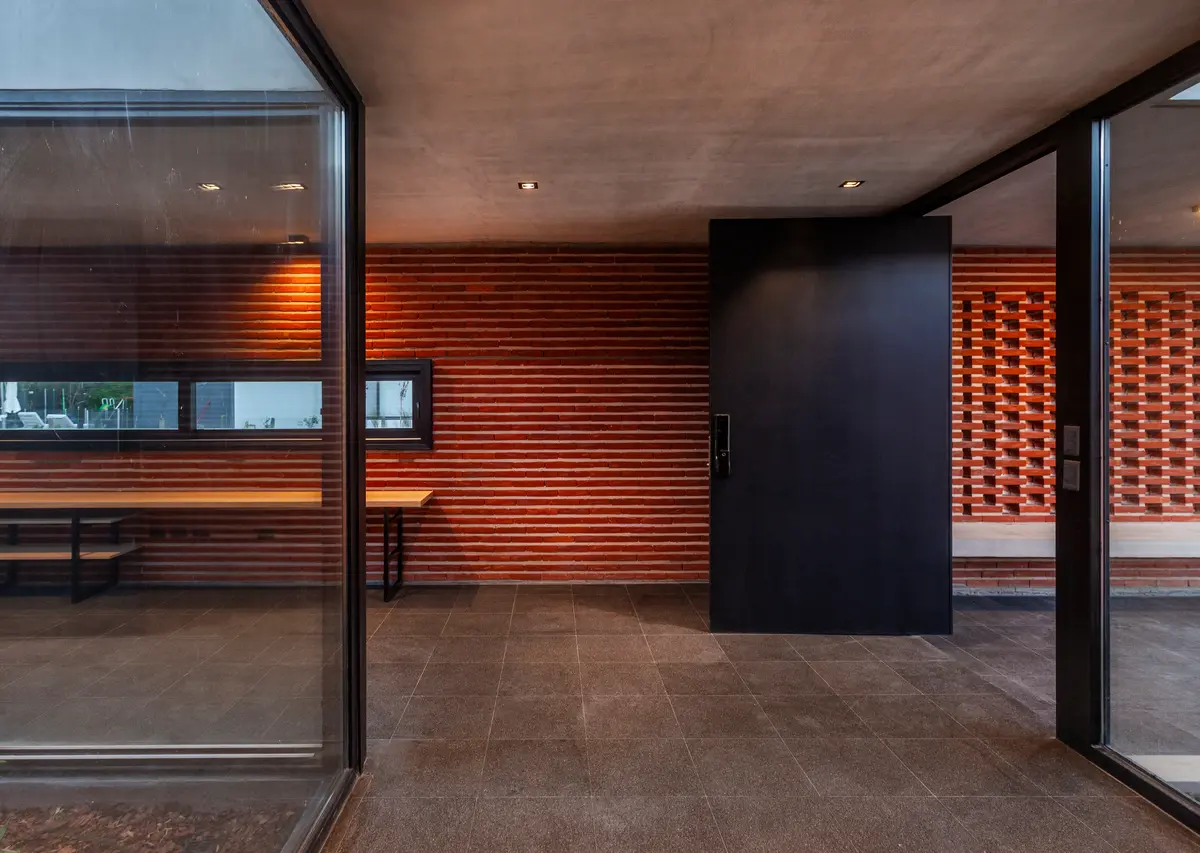 Entrada moderna com porta pivotante preta e tijolos horizontais — projeto Casa FLOIG, por V2 Arquitectos, em Villa Elisa