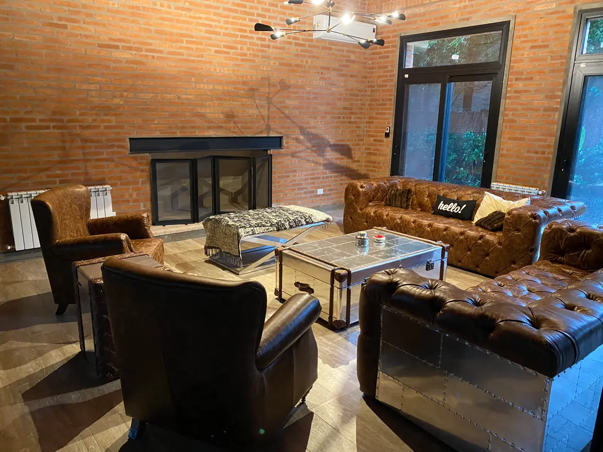 Sala de estar industrial com tijolos aparentes e poltronas de couro — projeto Loft y garage autos de colección, por Arq. Damian Fainzilber, em San Isidro