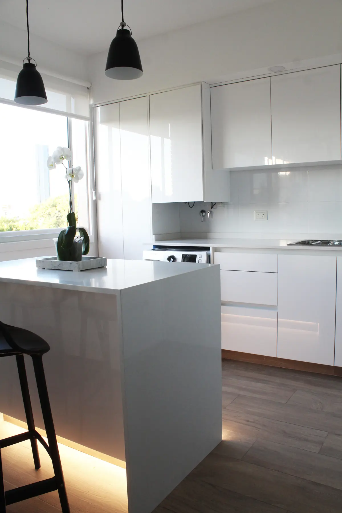 Cocina blanca minimalista con isla, piso madera y grandes ventanales — proyecto DEPTO OH, por Estudio Grupo 32, en Buenos Aires