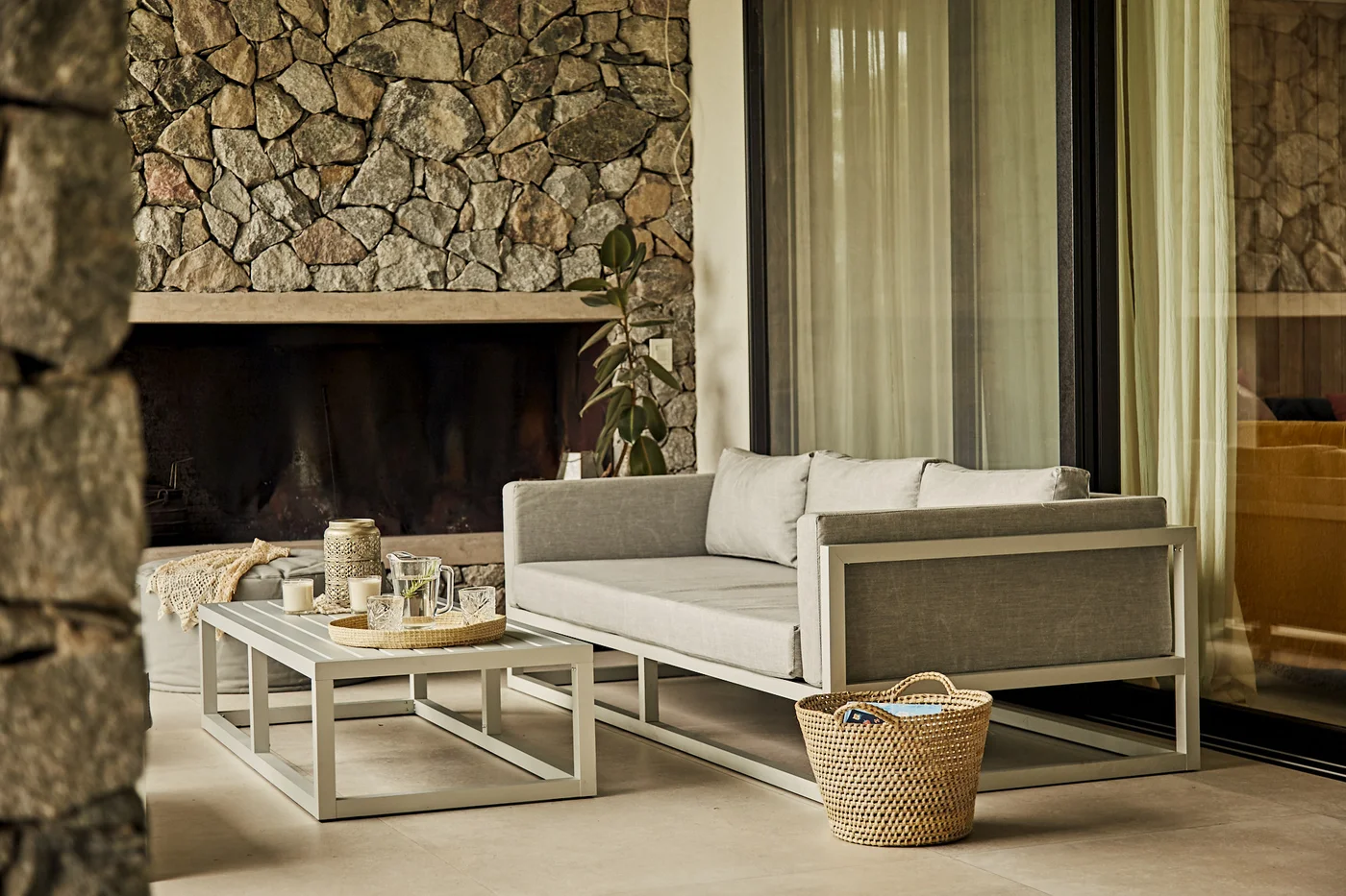 Terraza moderna con sofá gris, mesa baja y hogar de piedra