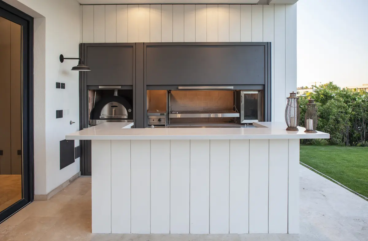 Quincho moderno con isla, parrilla integrada y vista al jardín — proyecto El Golf 137 - Nordelta, por Build a Home Arquitectura, en B1624 Tigre