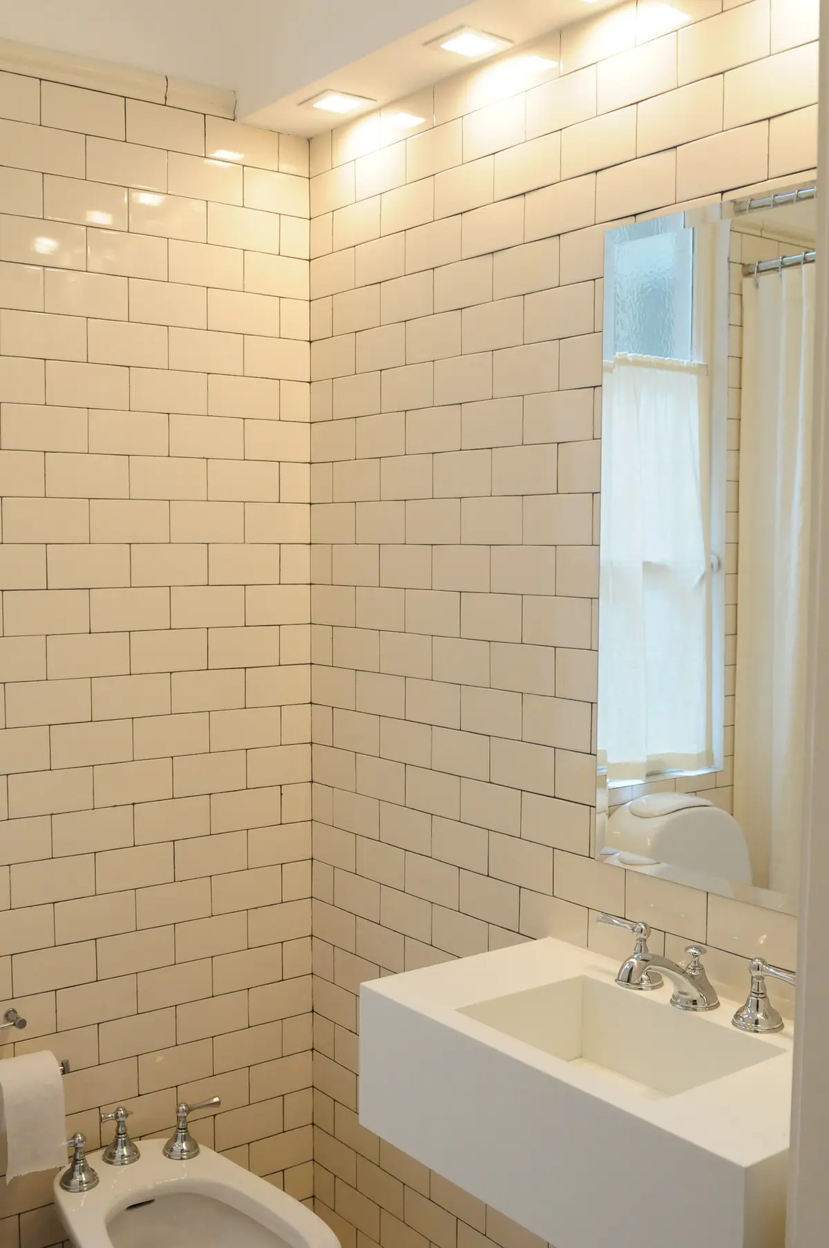 Banheiro moderno com azulejos bege, pia suspensa e iluminação indireta — projeto Dpto LH, por Estudio Dado, em Recoleta