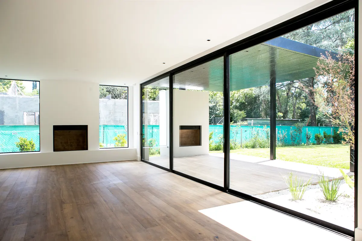 Sala de estar moderna com janelões e jardins, piso de madeira — projeto Bosque Chico, por Estudio Arq. María Sioli, em Garin