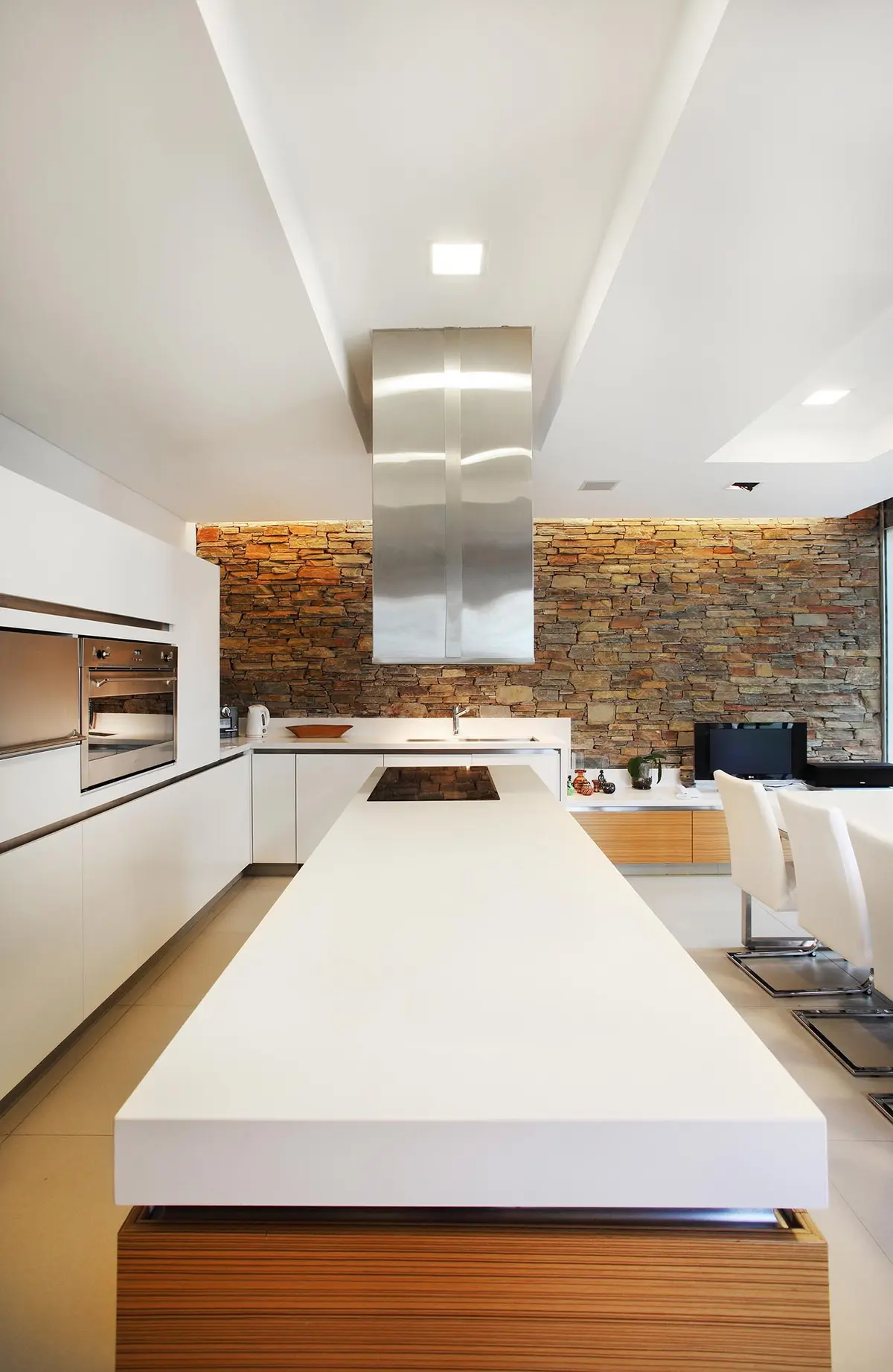 Cozinha moderna com ilha de pedra, parede de tijolos e móveis brancos — projeto Devoto, por Remy Arquitectos, em CABA