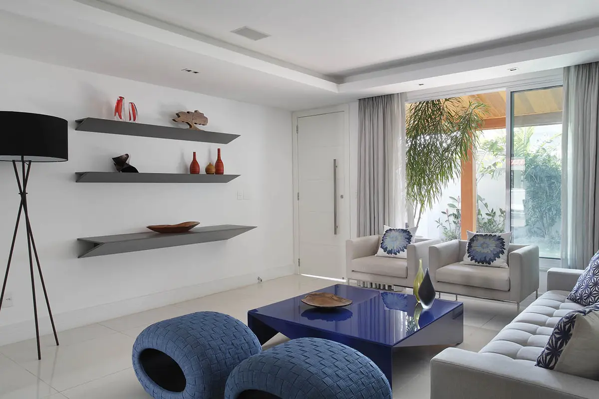 Living moderno con puffs azules, sofá gris y ventanal luminoso — proyecto Casa Barra ED, por Amanda Miranda