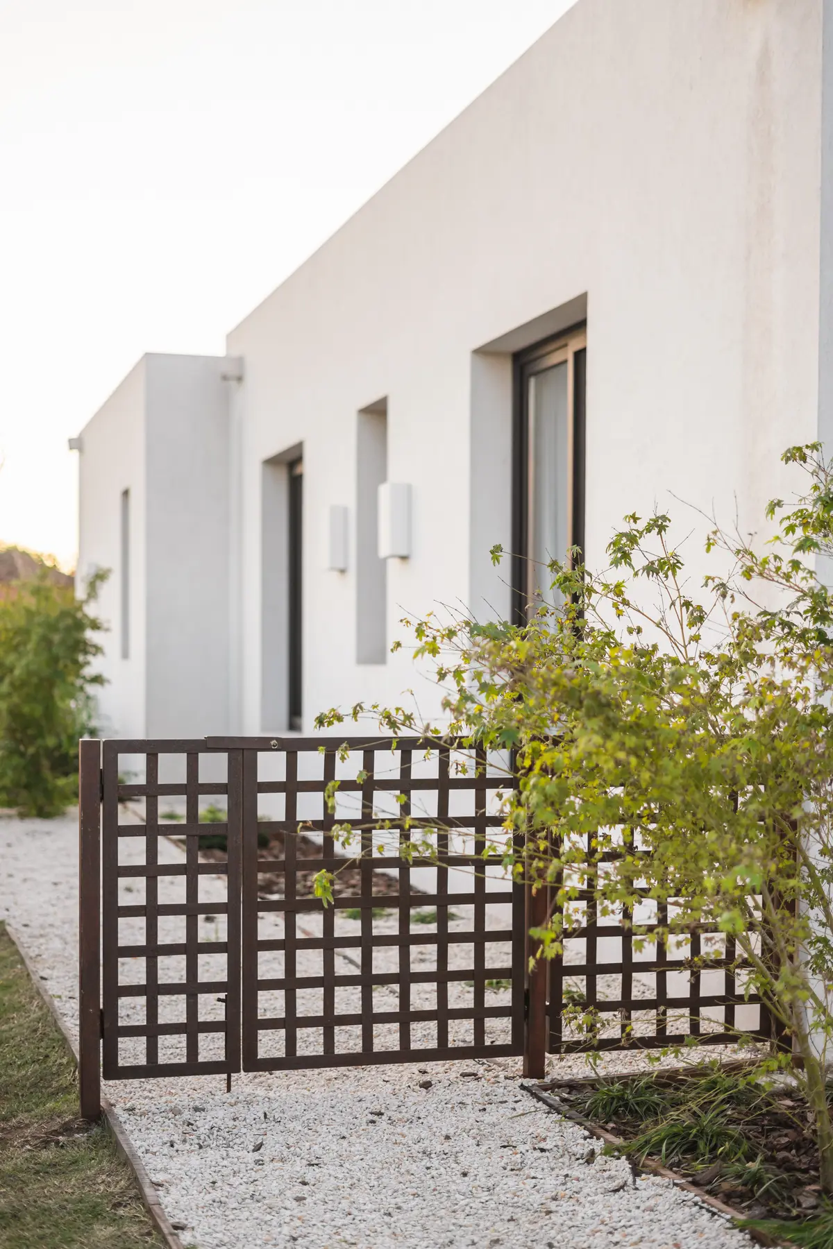 Casa moderna con portón de rejas de metal y fachada blanca — proyecto CASA PILARÁ, por CRUZ, en Pilará