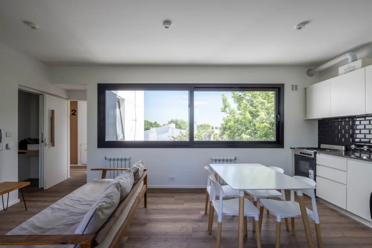 Living comedor cocina moderno con gran ventanal y muebles blancos — proyecto Terrazas de Saavedra, por DREI Arquitectura y Desarrollos, en La Plata