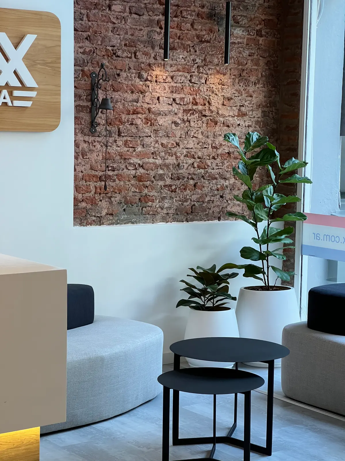 Sofá curvo cinza claro em frente à parede de tijolos expostos — projeto REMAX DEL PLATA, por Estudio Grupo 32, em Buenos Aires