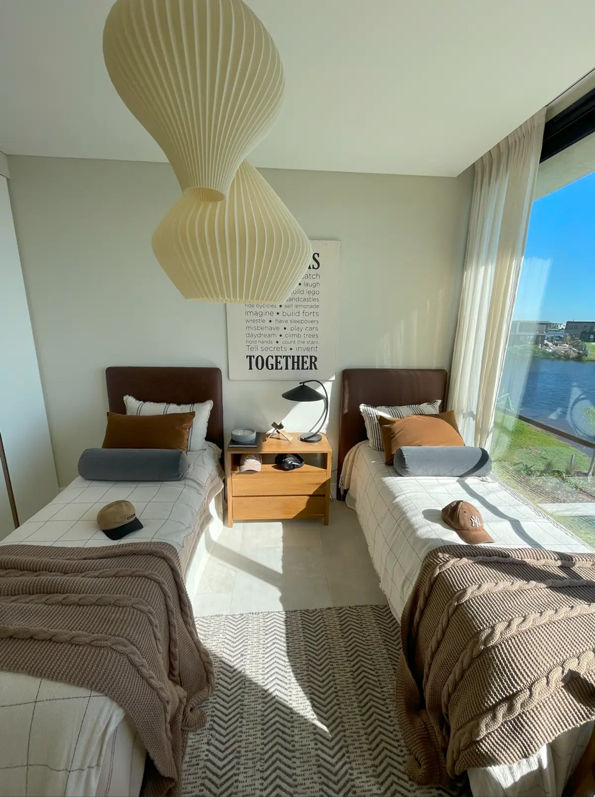 Dormitorio moderno con dos camas, grandes ventanales y lámpara colgante — proyecto El Secreto, por Grupo Pauta Arquitectura, en Tigre