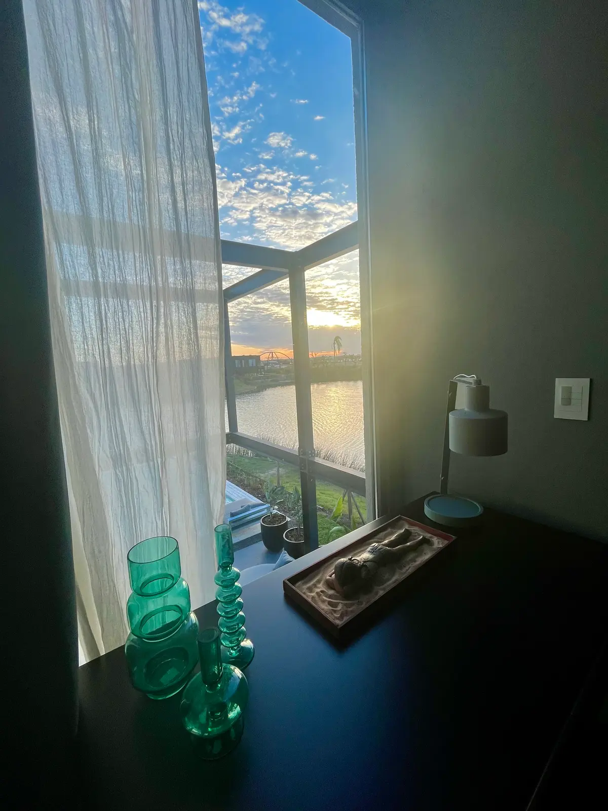 Sala moderna com janela grande e luz do pôr do sol, objetos de vidro verde — projeto Le chambre verte, por BRand arquitectura / BRand homes, em Belén de Escobar