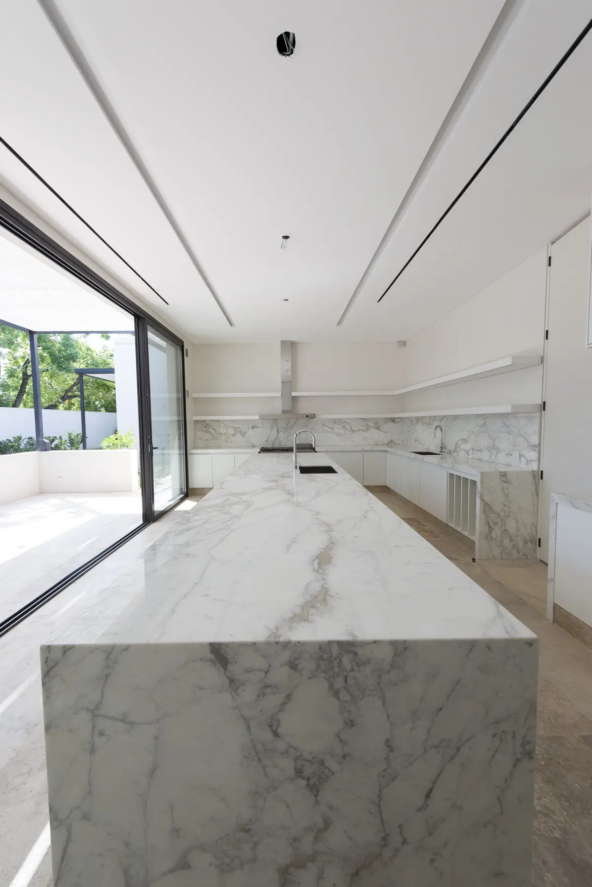 Cozinha moderna com ilha grande de mármore e janelas do chão ao teto — projeto Casa C, por Estudio Dado, em Belgrano