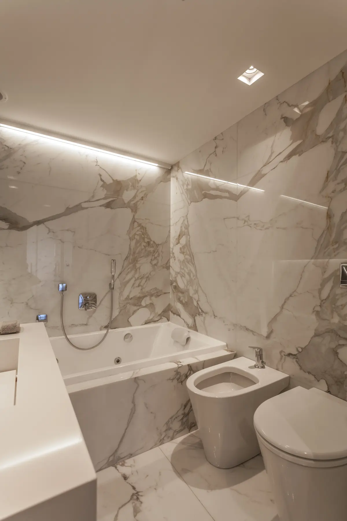 banheiro moderno com mármore branco, banheira de hidromassagem e bidê — projeto Le Parc, por Judith Babour, em CABA