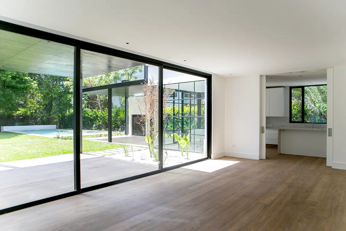 Sala de estar moderna com grandes janelas e vista para jardim com piscina — projeto Bosque Chico, por Estudio Arq. María Sioli, em Garin
