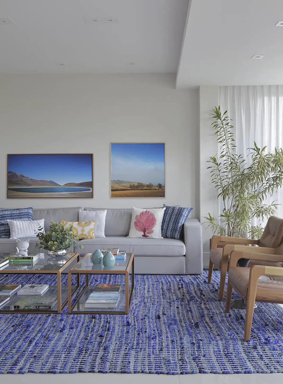 Living moderno con sofá gris, alfombra azul y mesas de vidrio — proyecto Apartamento Barra LM, por Amanda Miranda