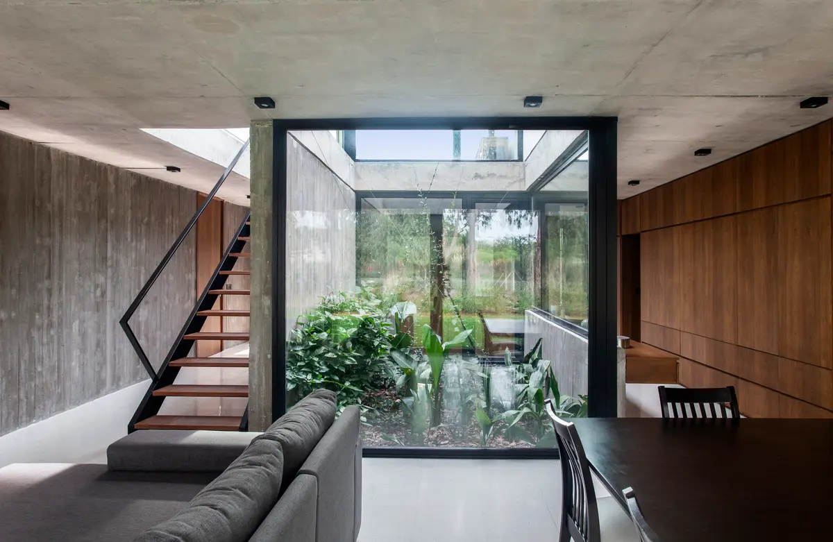 Sala moderna com pátio interno, escada flutuante e contraste de concreto e madeira — projeto Casa SRZ, por V2 Arquitectos, em City Bell