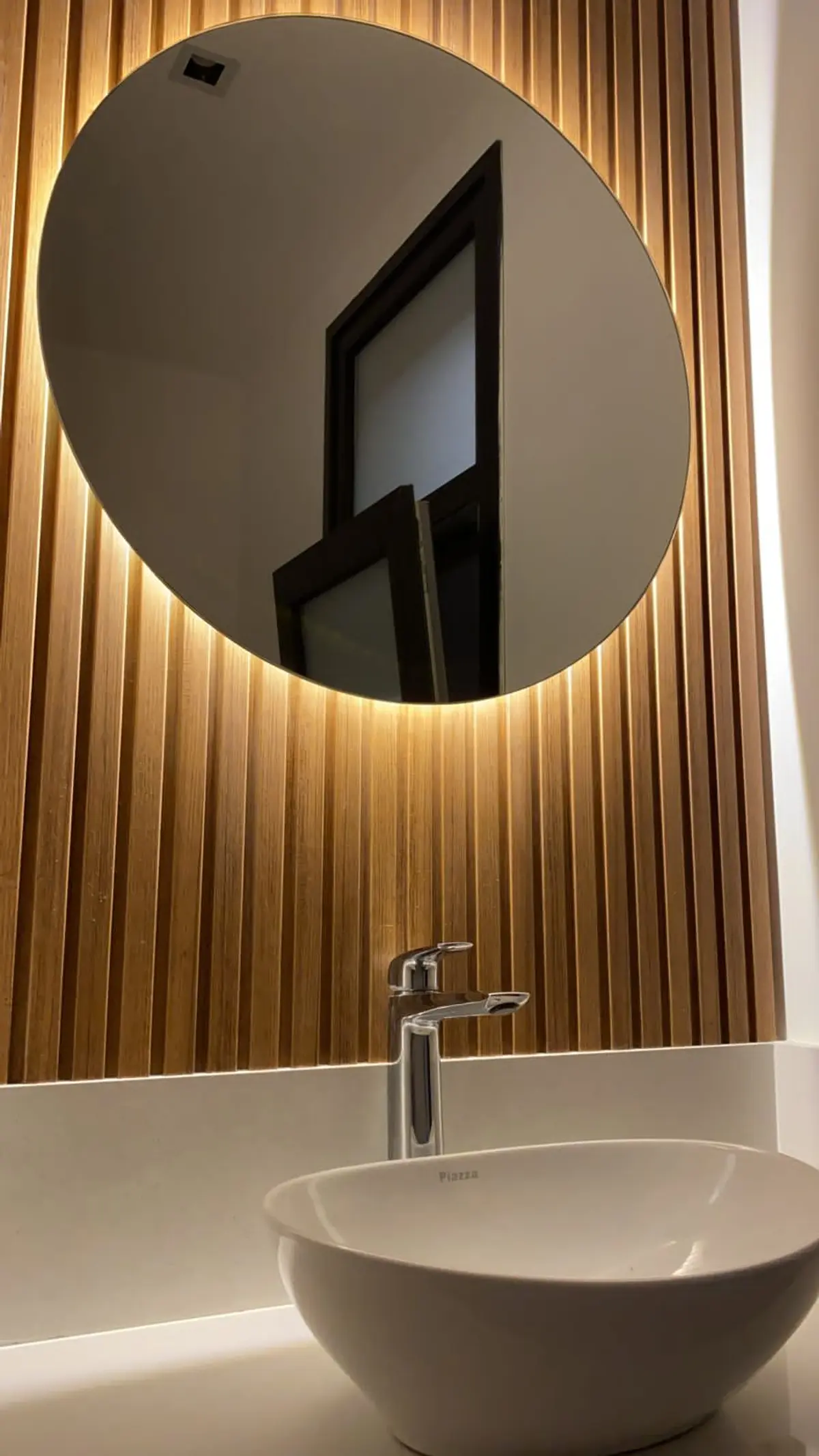 Baño moderno con espejo redondo retroiluminado y pared de lamas de madera — proyecto Casa Roy, por Arcucci Arquitectura, en Pilar