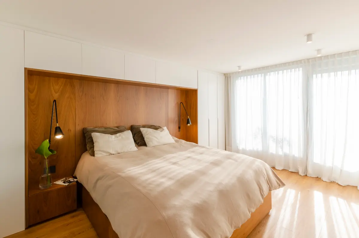 Dormitorio moderno con pared de madera, luz natural y cortinas blancas — proyecto Guayra - Andrea Gonzales, por ABEJA CONCEPT, en Belgrano