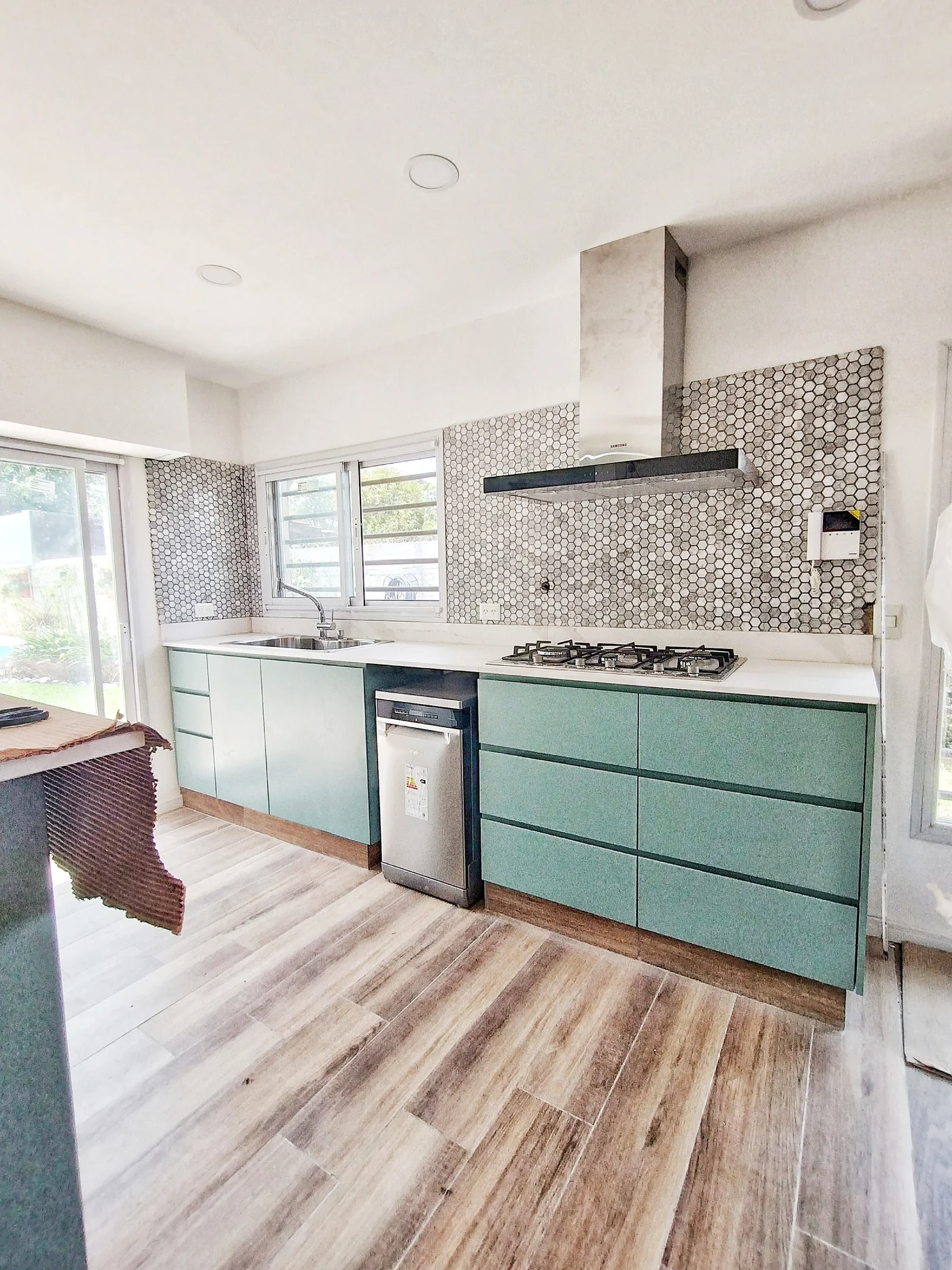 Cocina moderna escandinava con muebles verdes y piso símil madera.