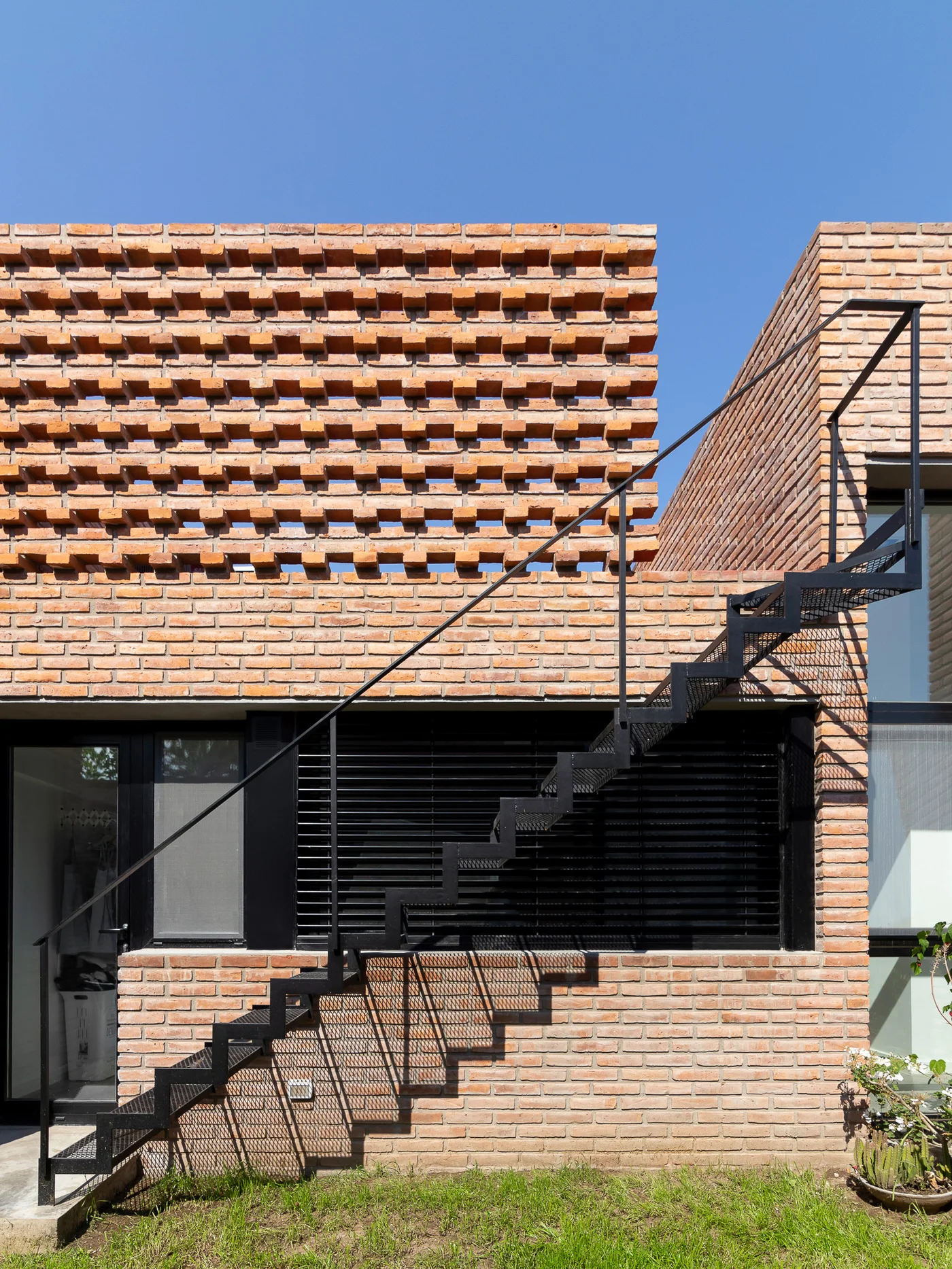 Fachada moderna con ladrillos texturizados y escalera metálica flotante.