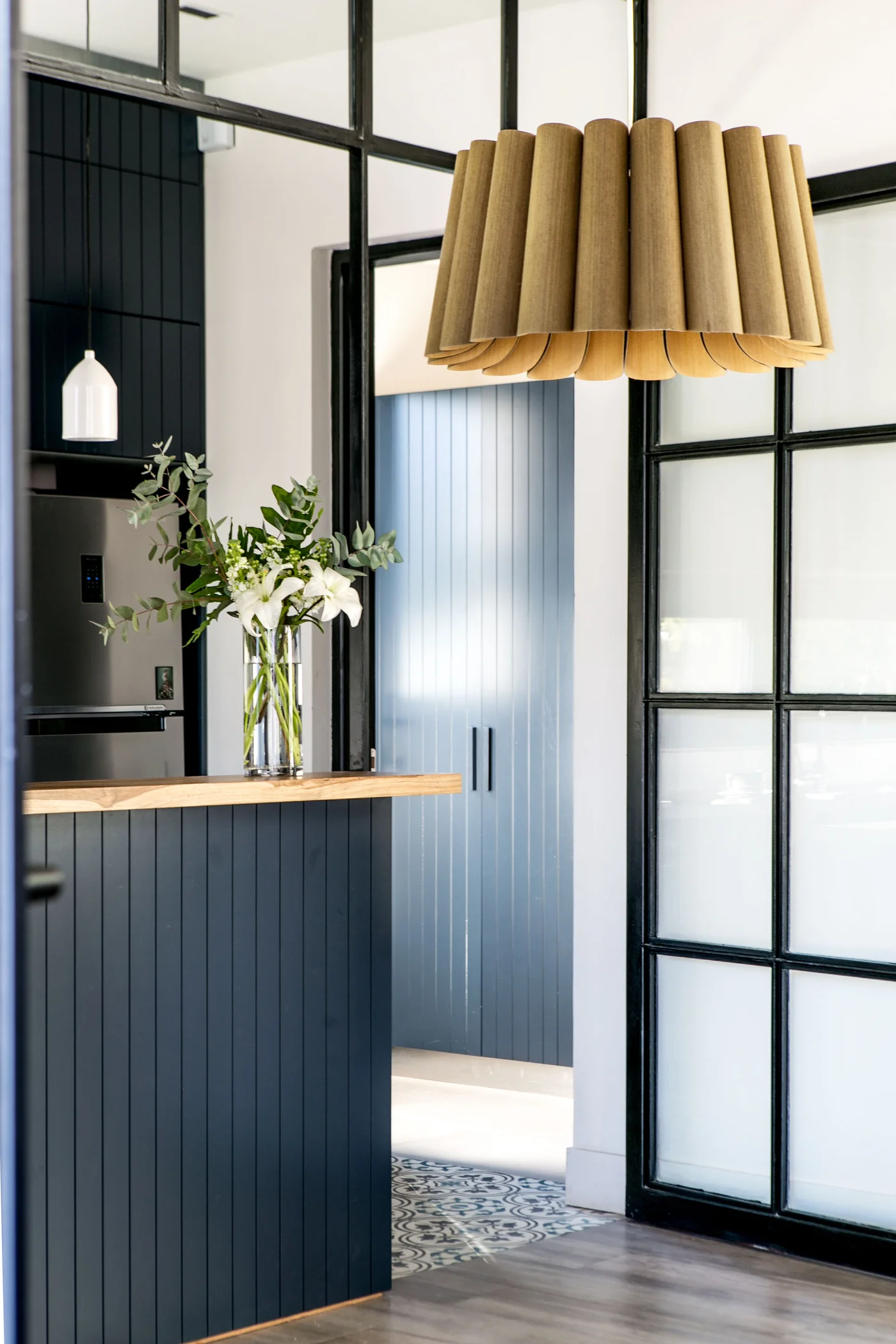 Cocina moderna con isla azul oscura, luz de tela plisada y madera.
