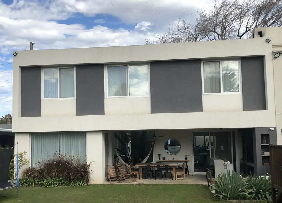 Fachada moderna con grandes ventanales y patio con muebles de rattan — proyecto LA HORQUETA, por Fb Arqs, en San Isidro
