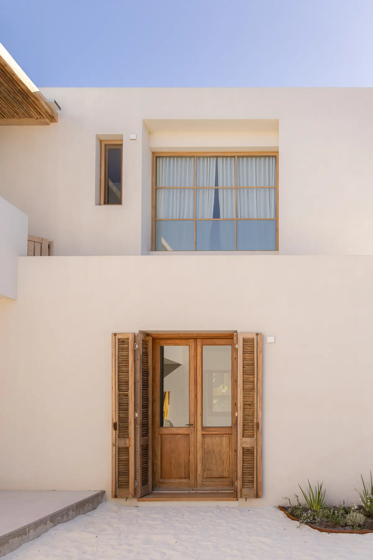 Fachada branca minimalista com portas de madeira e persianas — projeto El Refugio, por Grupo Pauta Arquitectura, em Pinamar