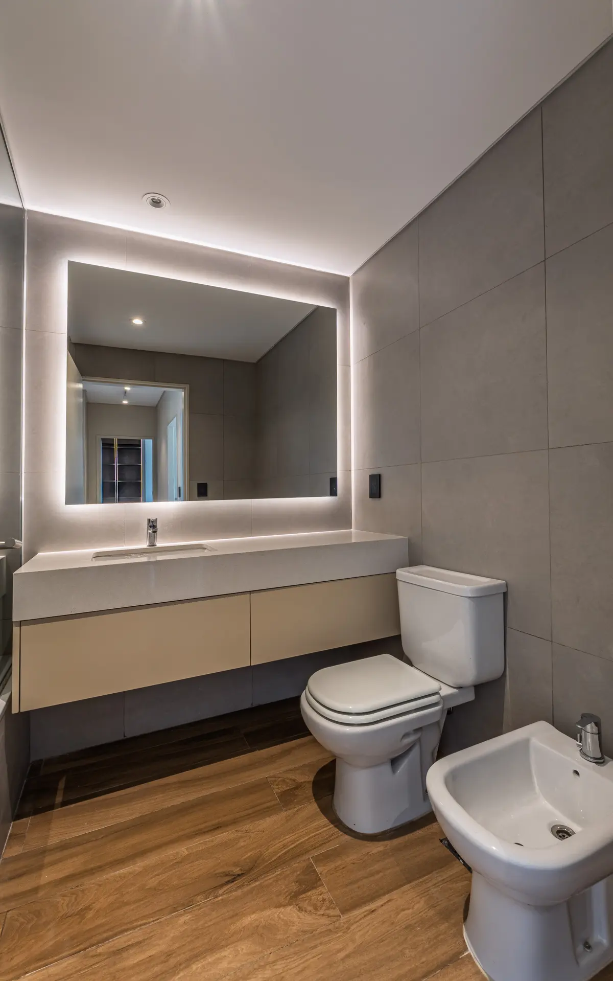 Baño moderno con espejo retroiluminado y piso de madera — proyecto Godoy Cruz, por ABEJA CONCEPT, en Palermo