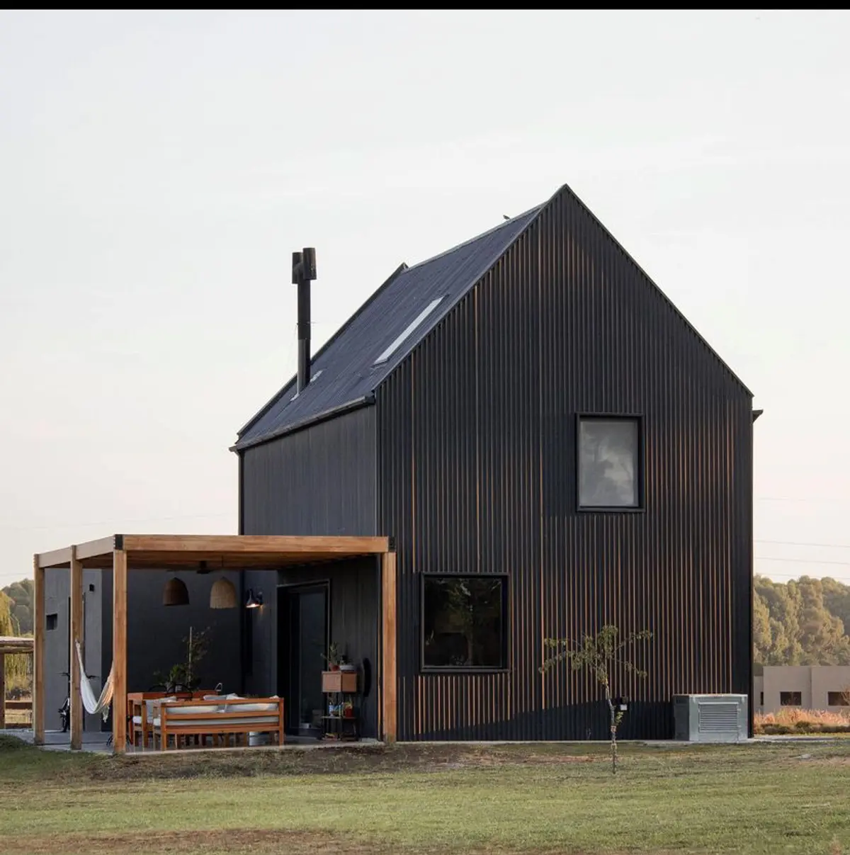 Casa moderna preta com pérgola de madeira e exterior rural — projeto Cabin, por Grupo Steimberg, em Pilar