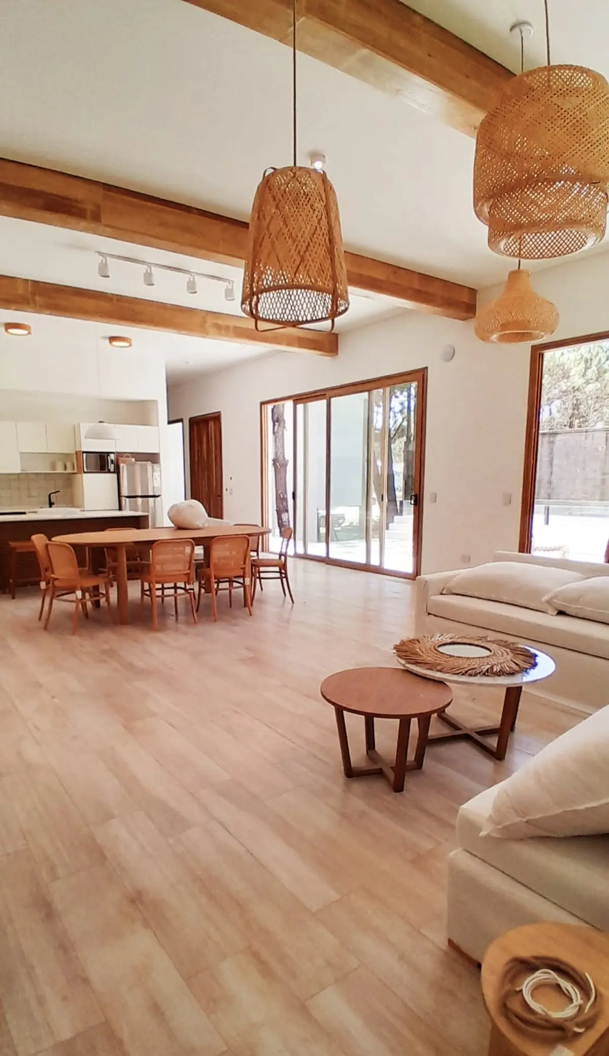 Sala de estar y comedor amplios con detalles en madera y luces tejidas — proyecto Casa NF, por TAVA Coop, en Pinamar