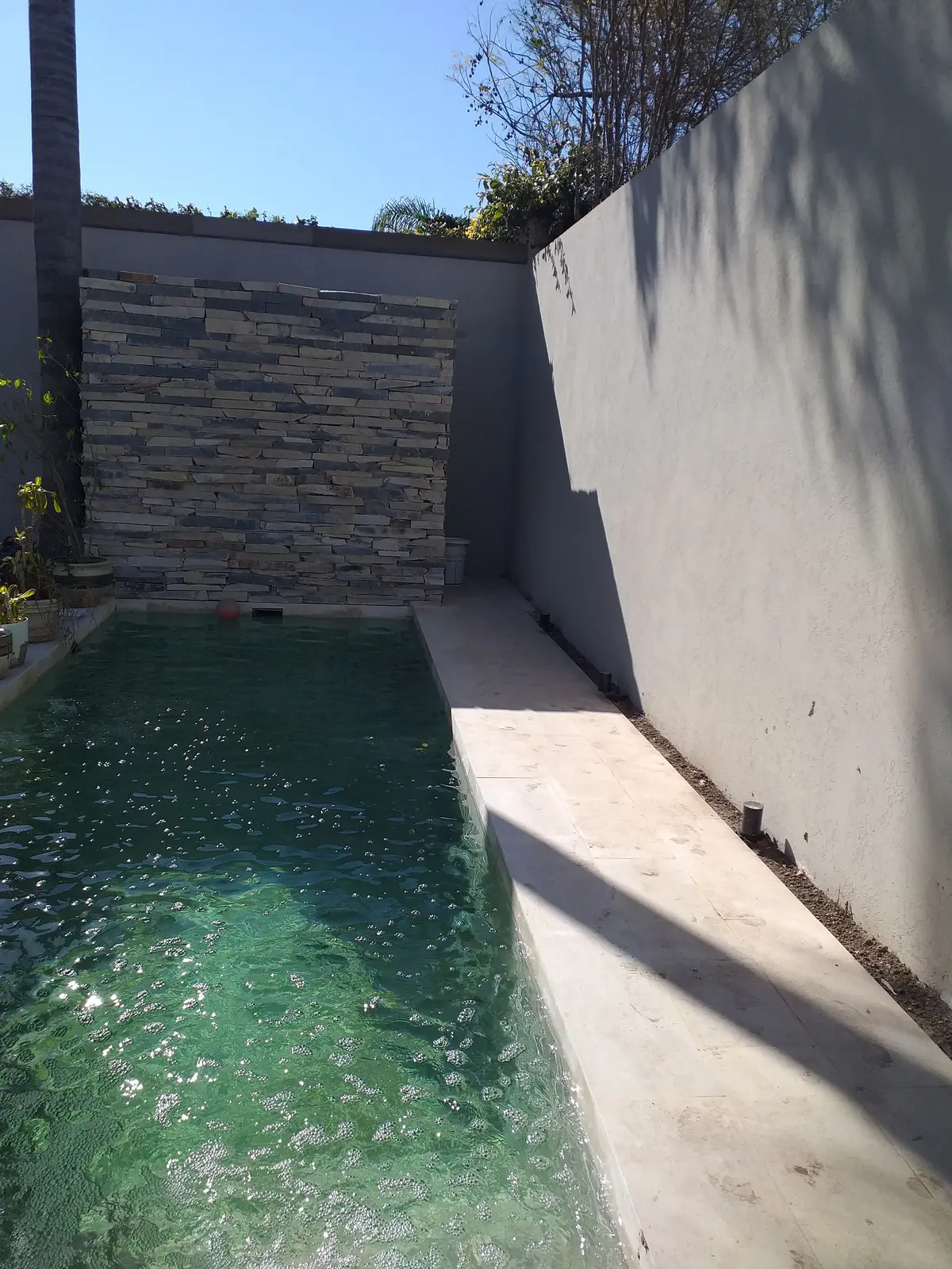 Piscina exterior con muro de piedra en cascada y borde de hormigón — proyecto Casa Estilo Francés, por Estudio Fernandez Long & asoc., en Martínez