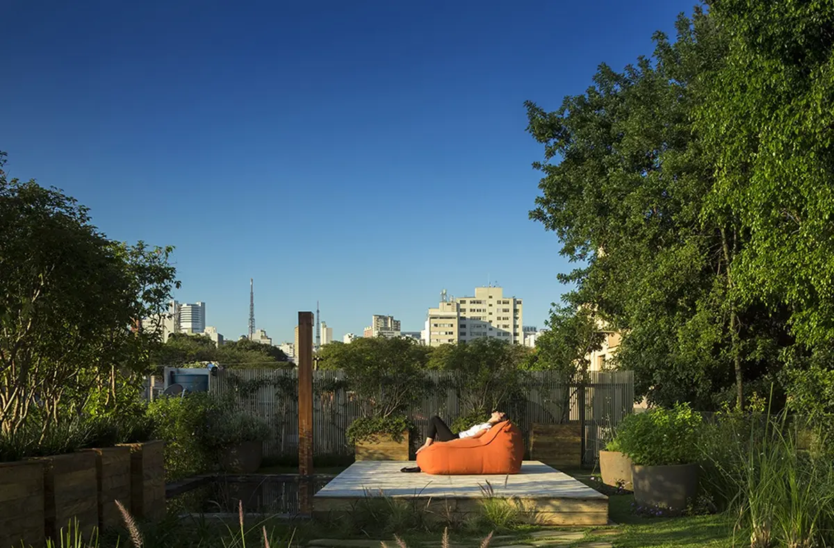 Patio con deck de madera, sillon naranja y vegetacion exuberante en Landhi — proyecto Residência AC, por Gil Fialho