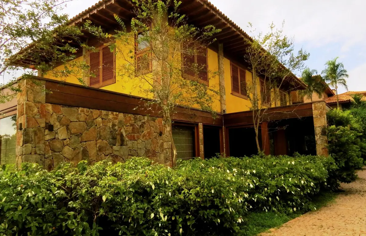 Casa amarilla rustica con piedra y vegetacion exuberante en fachada — proyecto Residência VL, por Gil Fialho