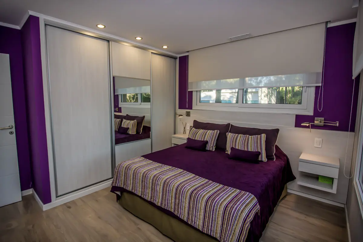 Quarto moderno com cama king, guarda-roupa branco e detalhes em roxo — projeto Vivienda Unifamiliar en Pinamar, por Estudio Schifano, em Pinamar