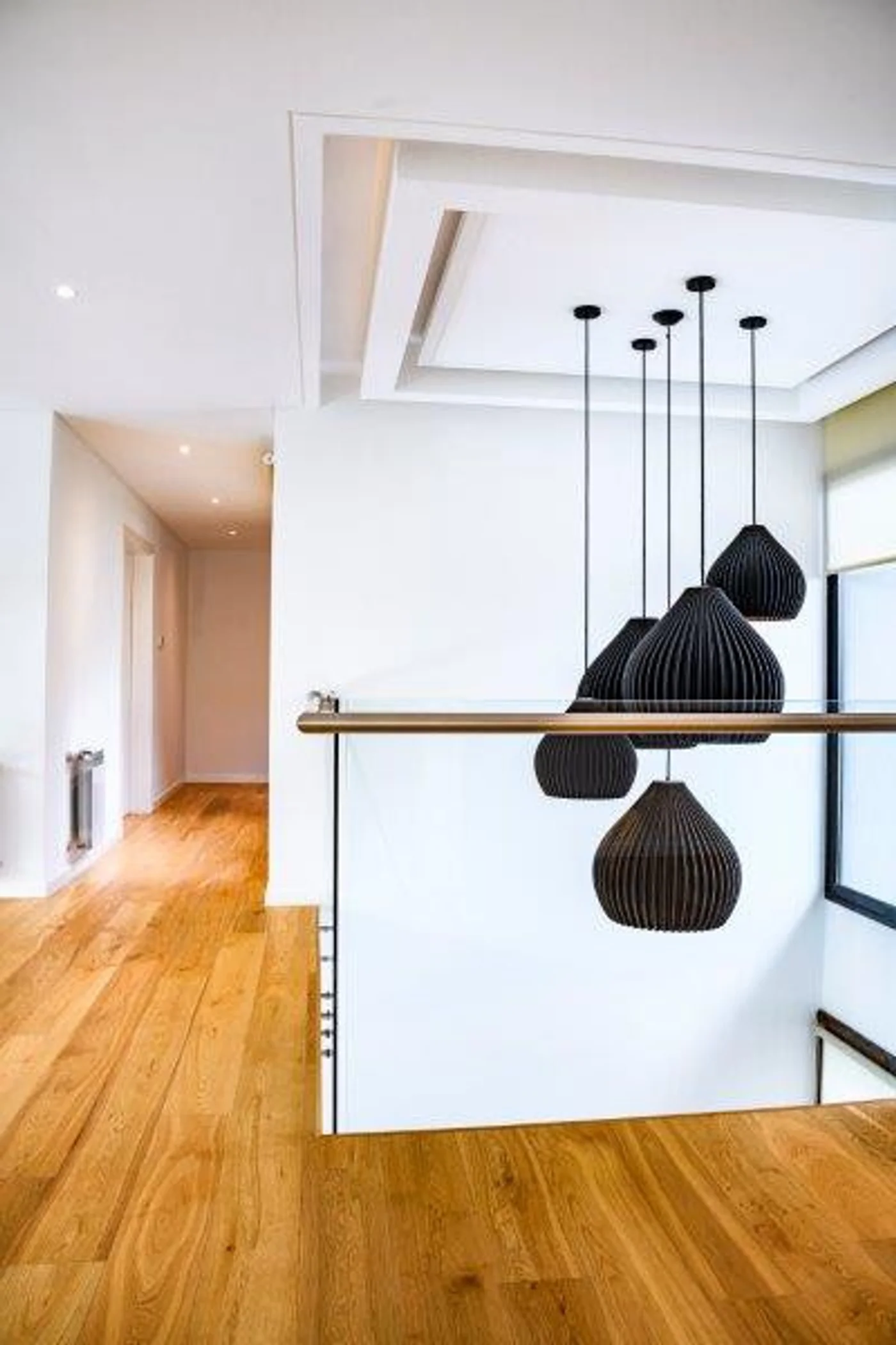 Pasillo moderno con luces colgantes negras y suelo de madera