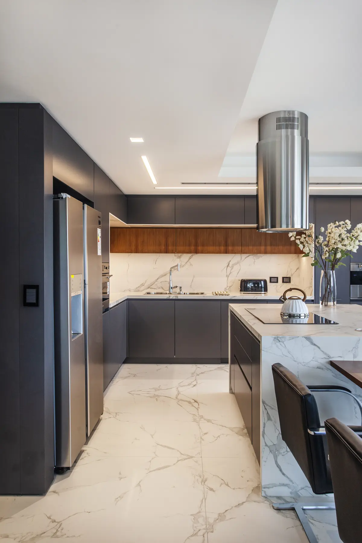 Cocina moderna con isla de mármol, muebles oscuros y grises, iluminación indirecta — proyecto Pacífico BRT, por Vanguarda Arquitectos, en CABA