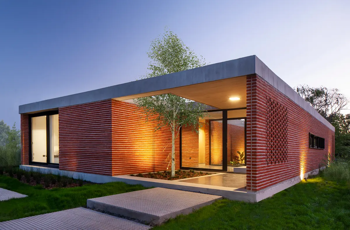 Casa moderna com fachada de tijolo e madeira, pátio interno e telhado em balanço — projeto Casa FLOIG, por V2 Arquitectos, em Villa Elisa