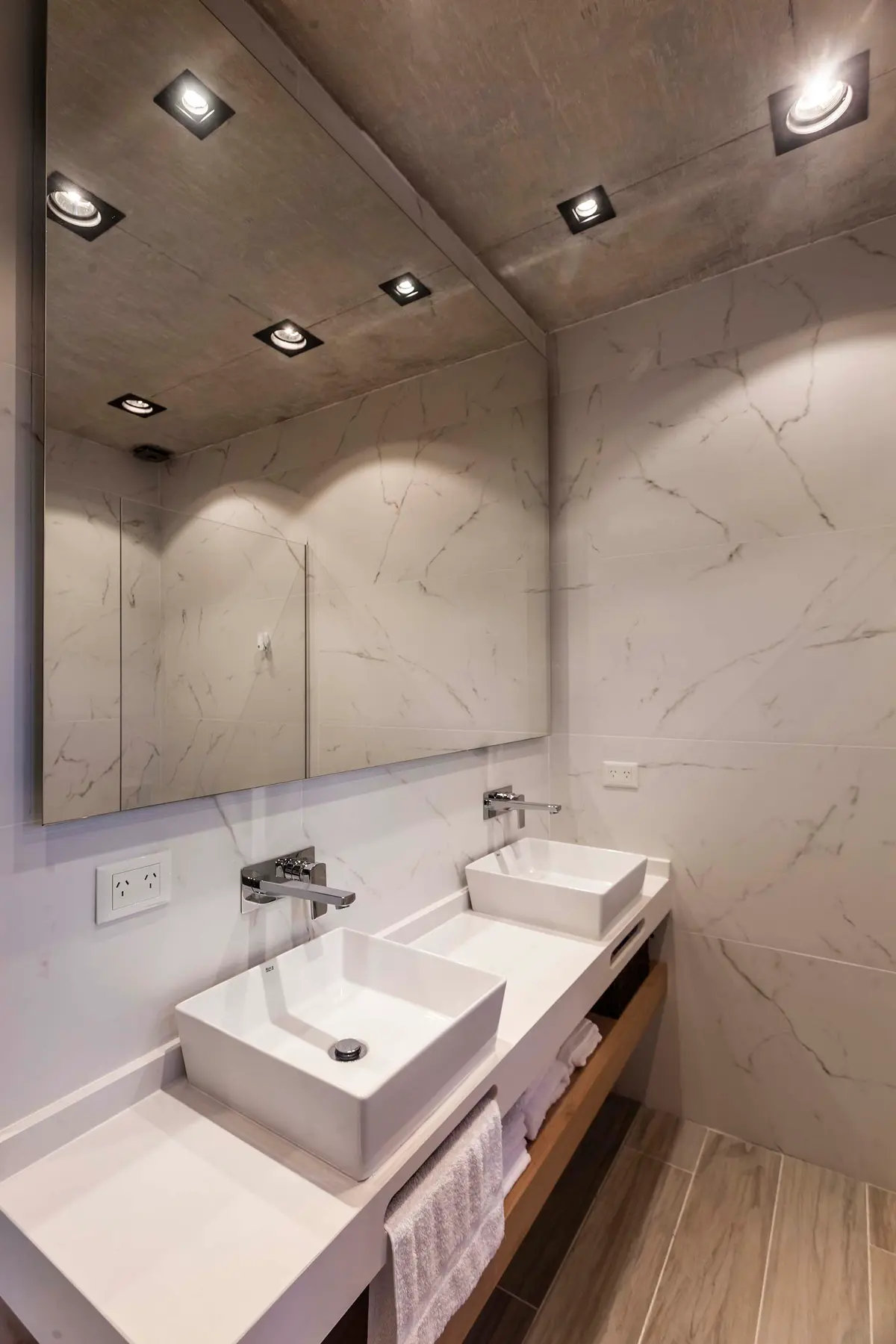 Banheiro moderno com duas cubas retangulares sobre bancada de microcimento e parede de mármore — projeto DISEÑO INTERIOR - CASA VISTAS, por FOCO_arquitectura&diseñointerior, em Bel