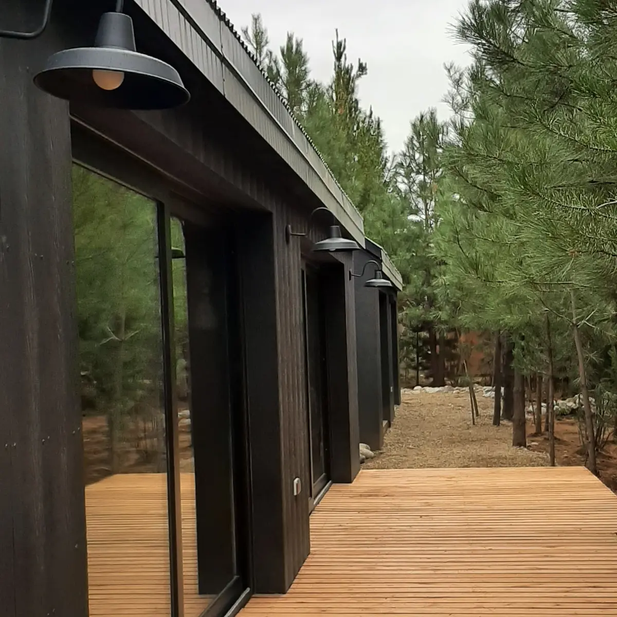 fachada moderna em madeira escura com deck e luminárias — projeto Casa LA MOROCHA, por Showhouse Bariloche, em San Carlos de Bariloche