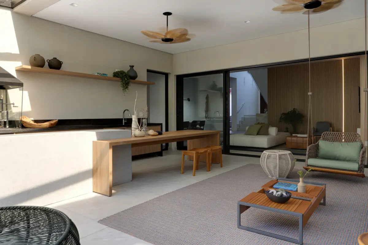 Ampla sala de estar e cozinha integrada com mesa de madeira e cadeiras suspensas de rattan — projeto Projeto Destaque Club&Casa, por Barbara Dundes – Arquitetura + Design