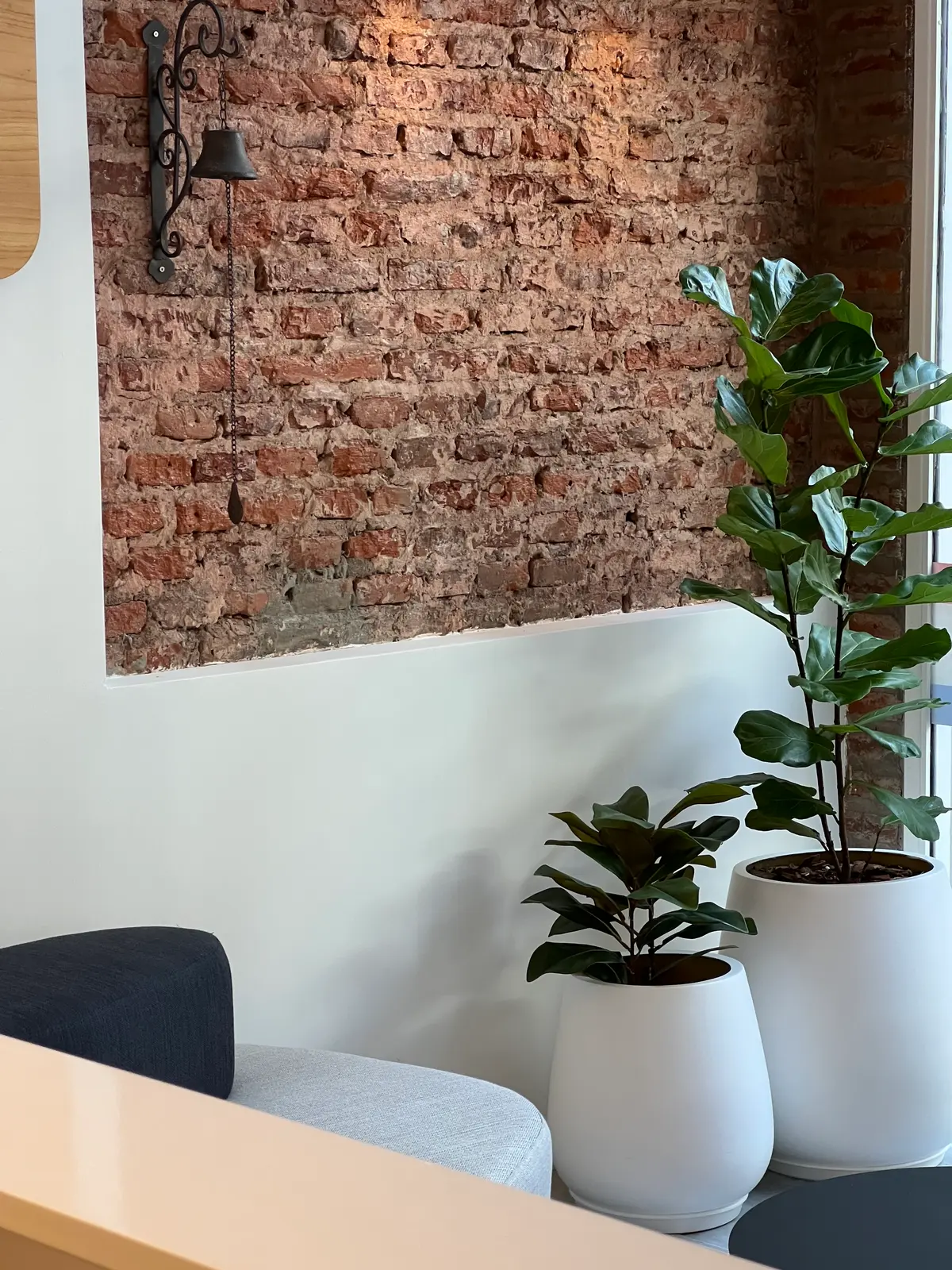 Parede de tijolos expostos com sino antigo e plantas modernas — projeto REMAX DEL PLATA, por Estudio Grupo 32, em Buenos Aires