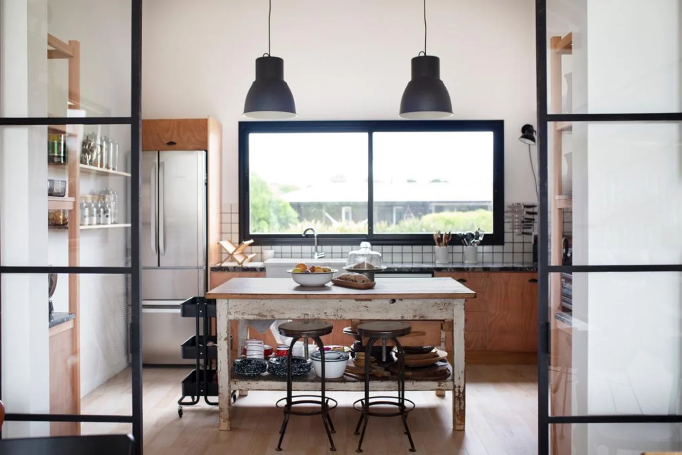 Cocina moderna con isla de madera, ventanal amplio y lámparas colgantes negras