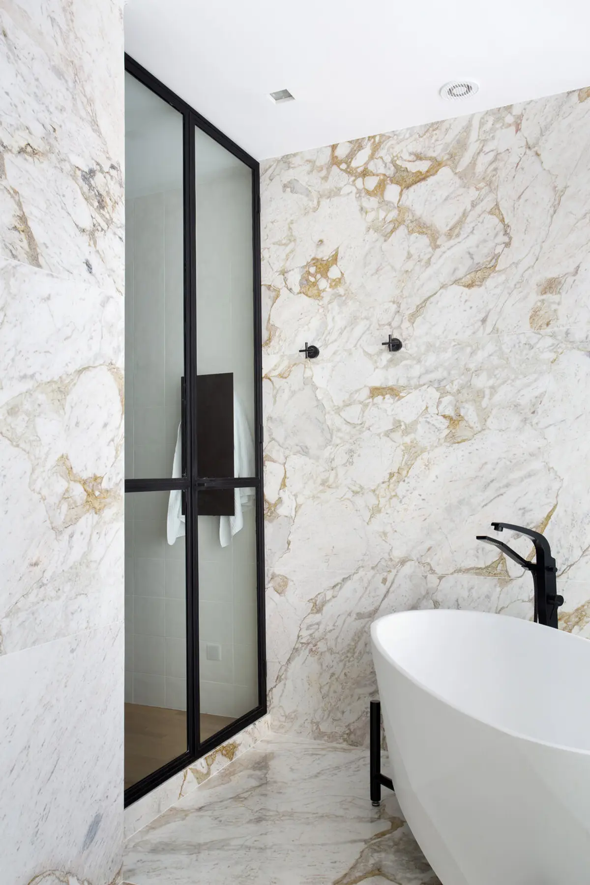 Baño moderno con mármol blanco, bañera blanca y mamparas negras — proyecto BM House, por Studio Ro-ca